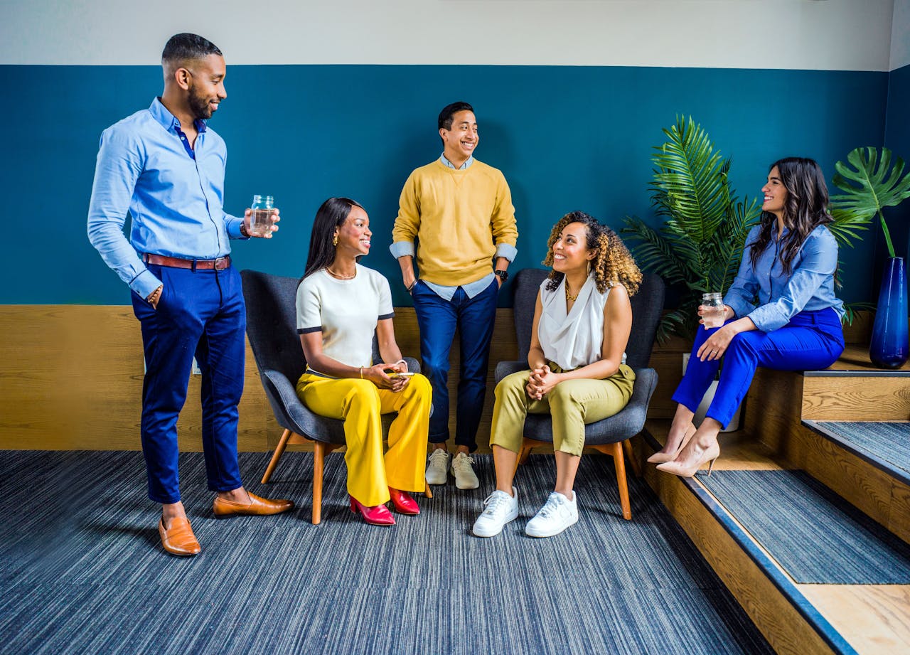 about-hero A diverse group of five professionals engaging in a casual indoor meeting, smiling and talking.