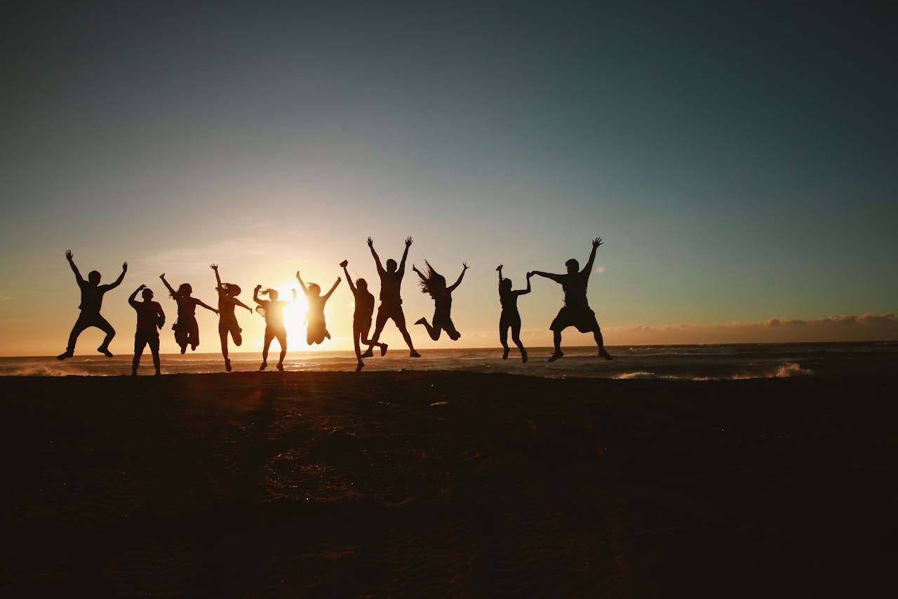 why-choose-us Silhouette of a group of friends jumping on a beach at sunset, expressing joy and freedom.